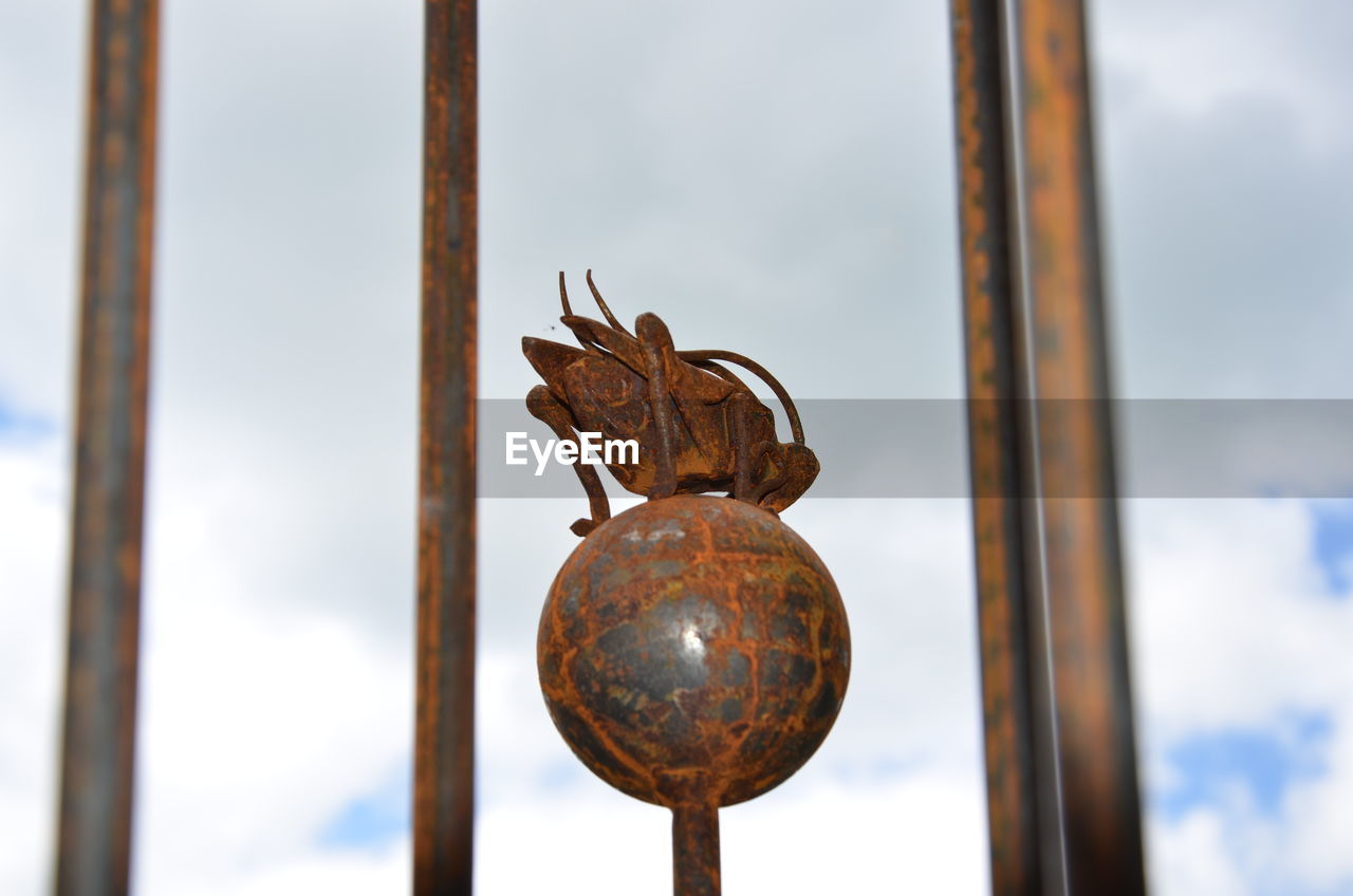 Rusty metallic cricket and sphere sculpture against sky