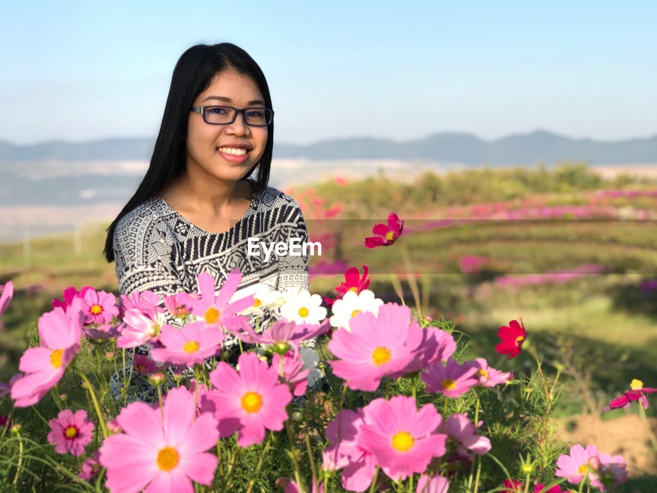 Portrait of smiling woman by flowering plants on field