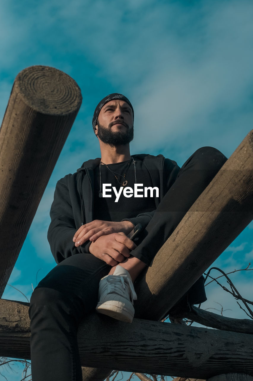 Low angle view of thoughtful man sitting on wood against sky