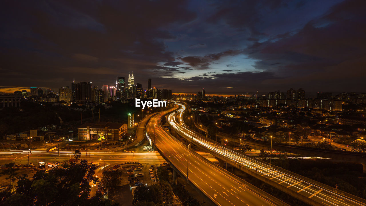 HIGH ANGLE VIEW OF LIGHT TRAILS ON ROAD AMIDST BUILDINGS IN CITY