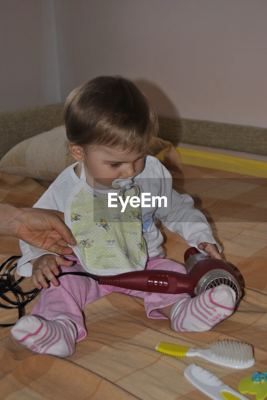 Cropped hand of mother holding boy playing with hair dryer on bed at home