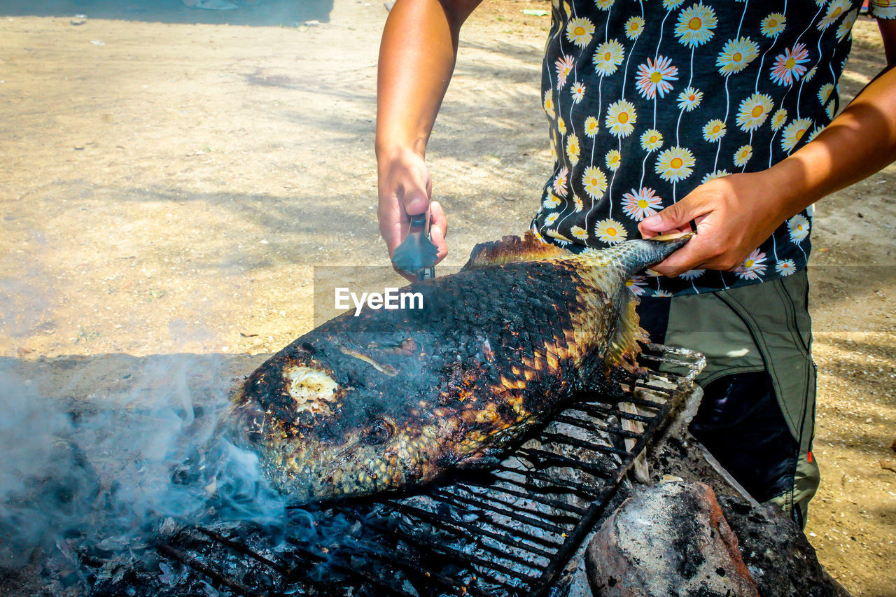 Midsection of man cooking fish on barbeque