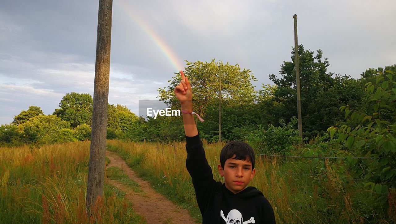 Optical illusion of boy holding rainbow while standing on field