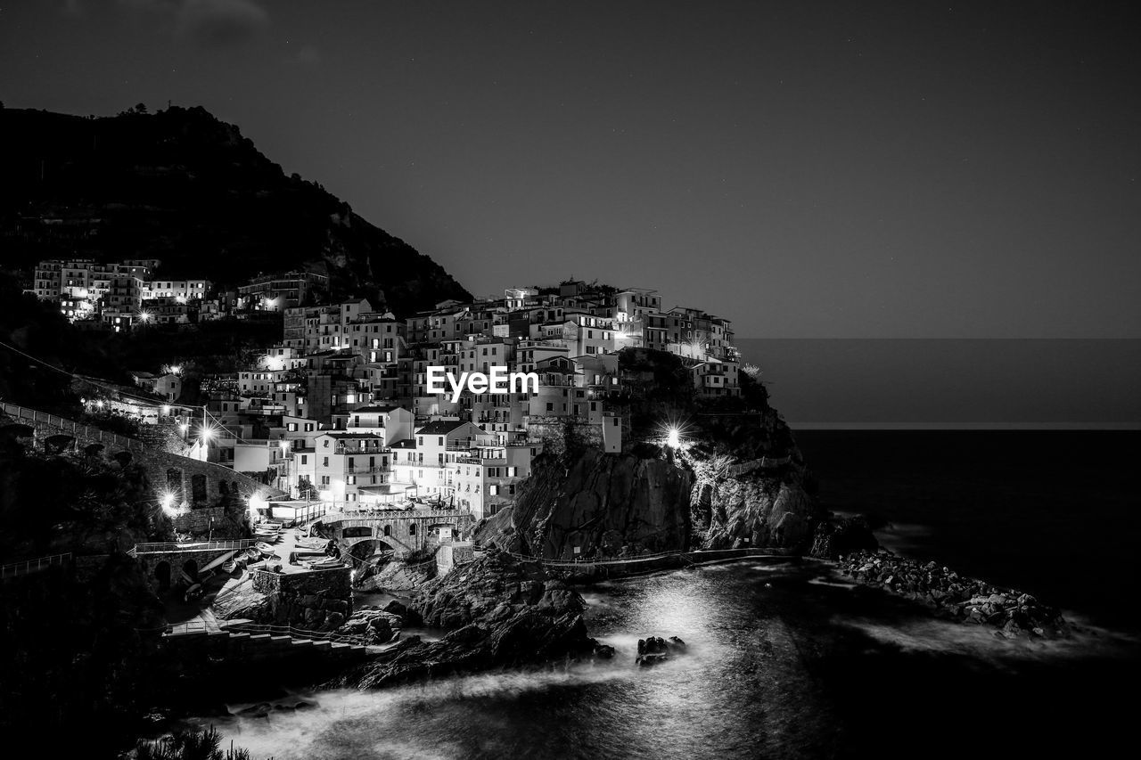 Illuminated manarola at sea shore against clear sky during dusk