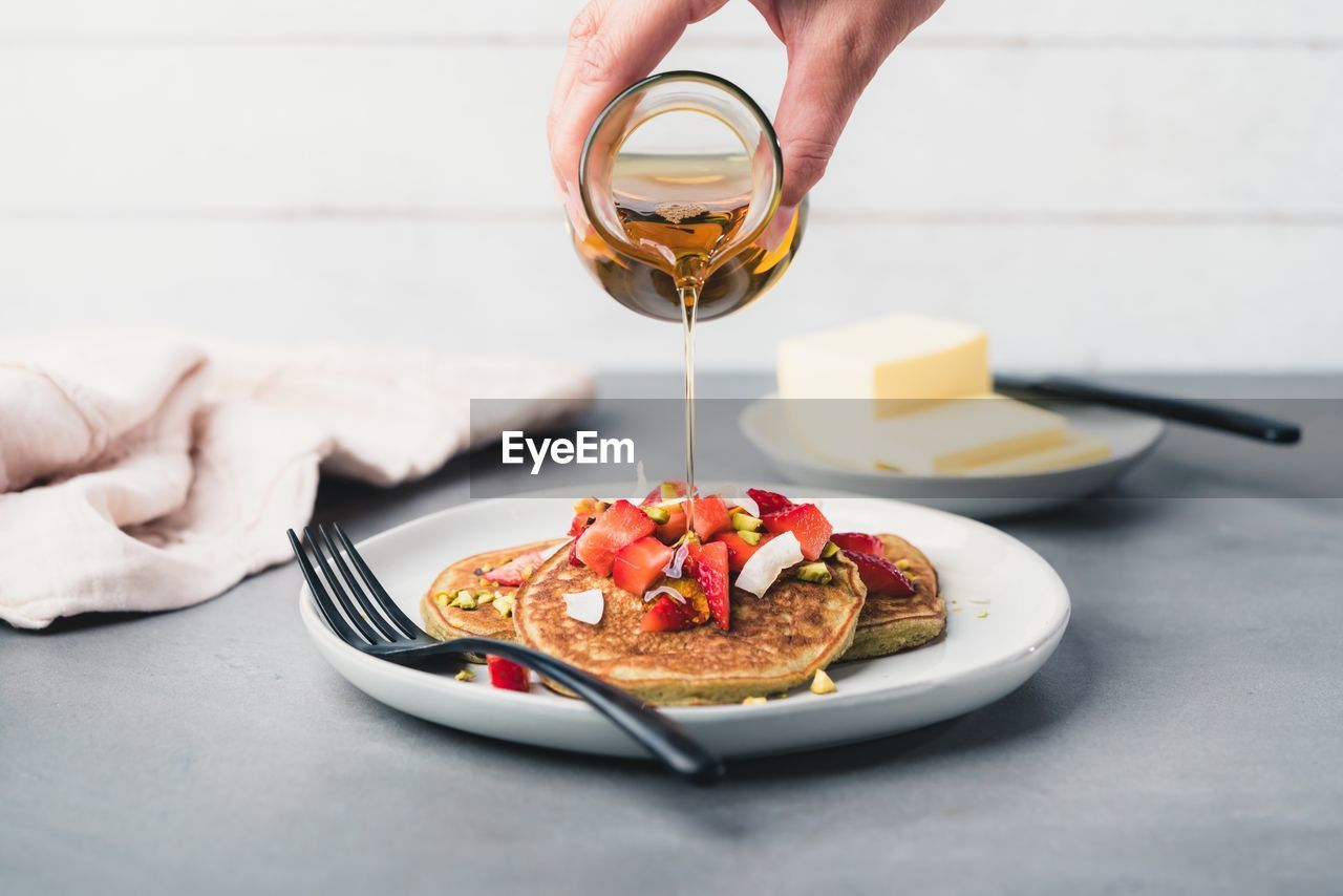 Cropped hand of person pouring honey on meal in plate