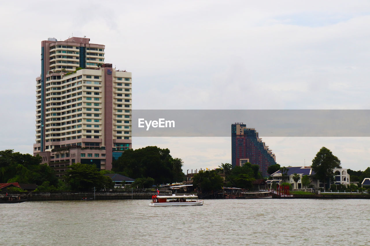 BOAT ON RIVER BY BUILDINGS AGAINST SKY