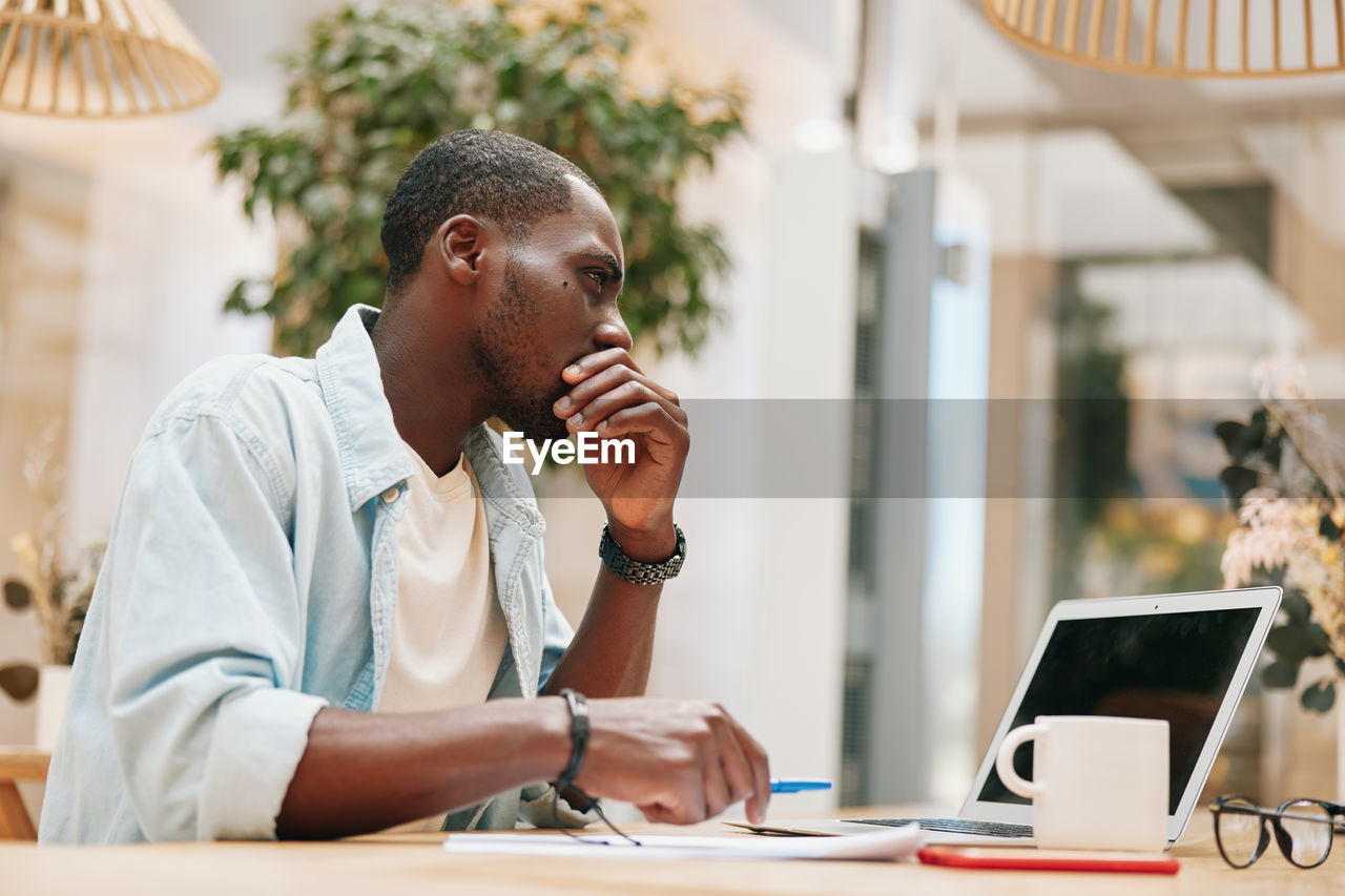 side view of young man using mobile phone while sitting in cafe