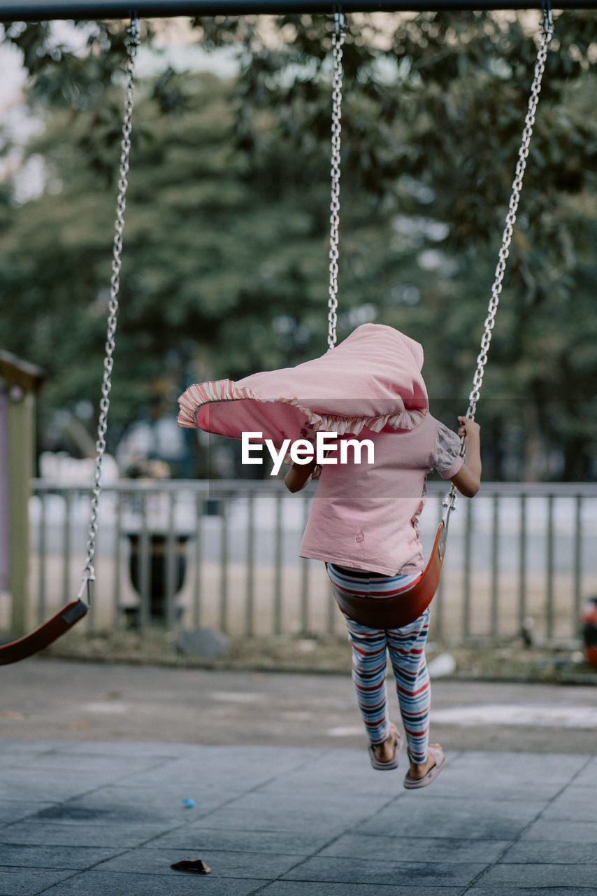 full length, childhood, swing, spring, one person, playground, child, day, casual clothing, rear view, chain, focus on foreground, outdoors, lifestyles, nature, female, leisure activity, architecture, toddler, women, outdoor play equipment, hanging, rope, baby, motion, footwear