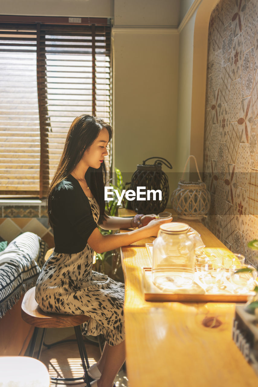 Side view of young woman sitting on table at home