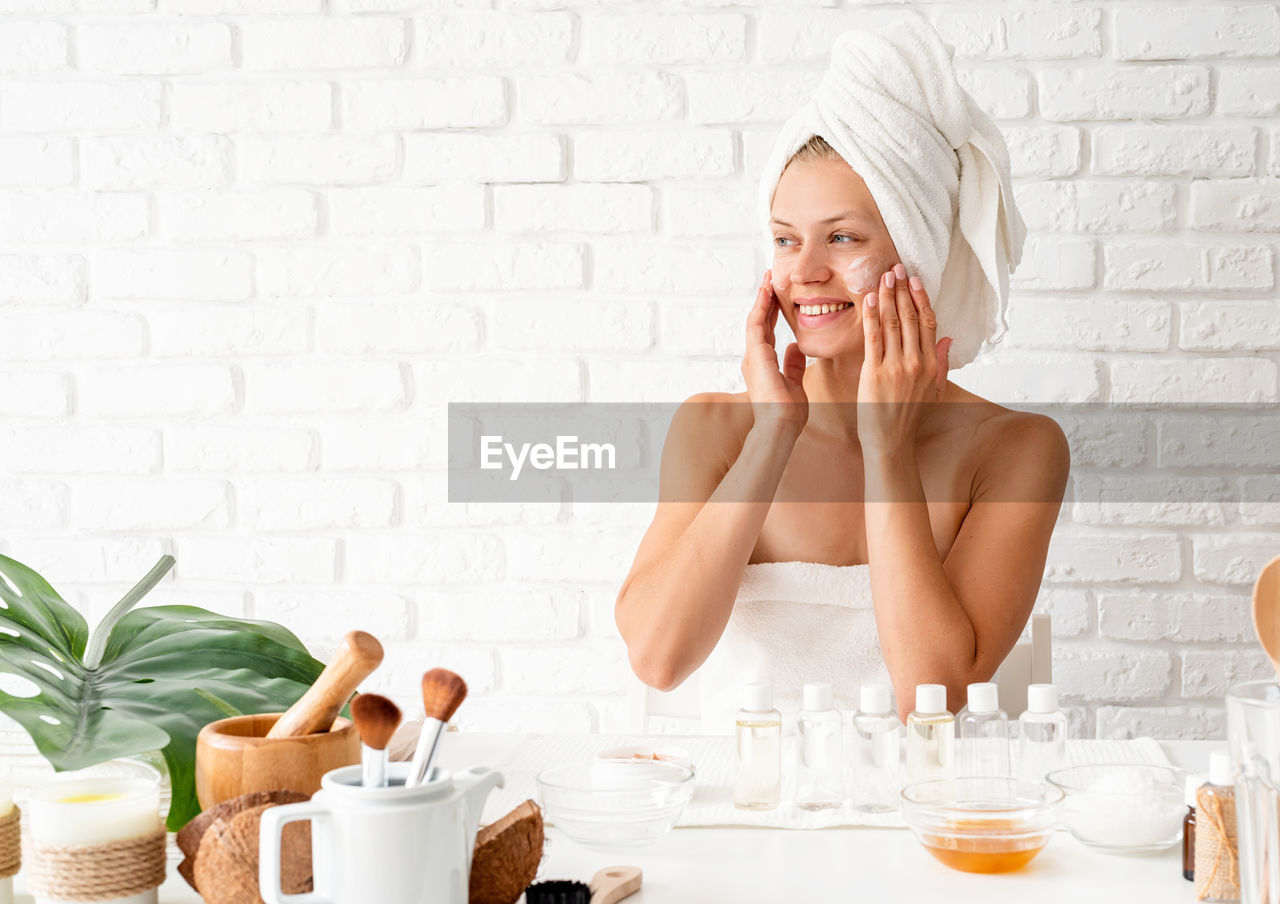 Natural cosmetics. happy young woman in white bath towels applying face cream doing spa procedures