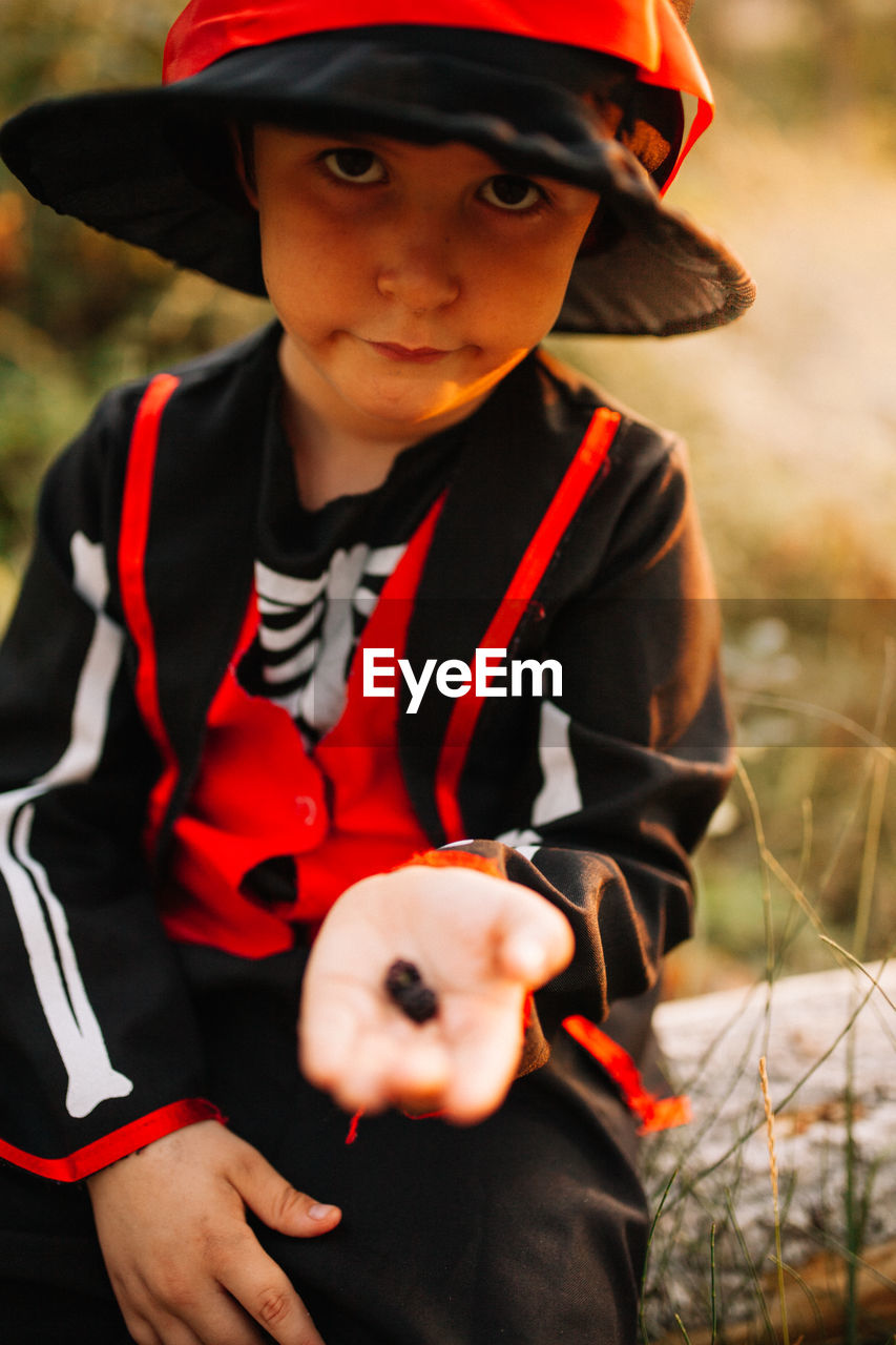 Portrait of boy wearing costume during halloween holding blackberries at forest