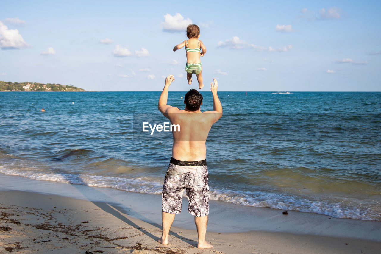 Rear view of of a man throwing a young child up into the air