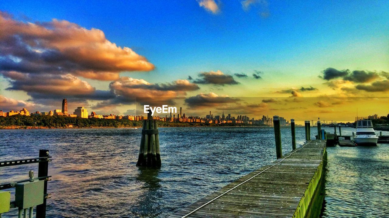 Pier on sea by cityscape against sky during sunset