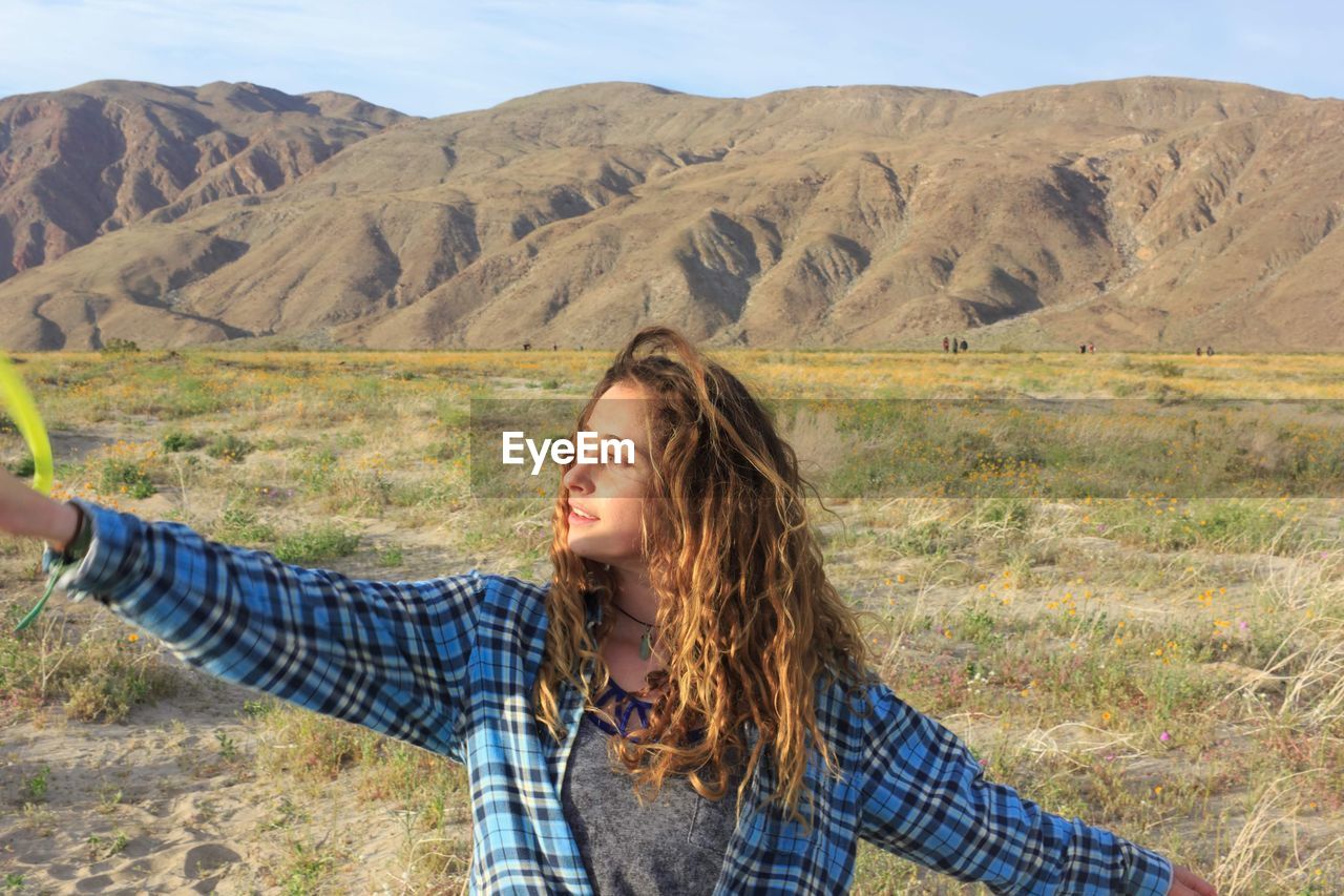 Woman with arms raised looking away against mountains