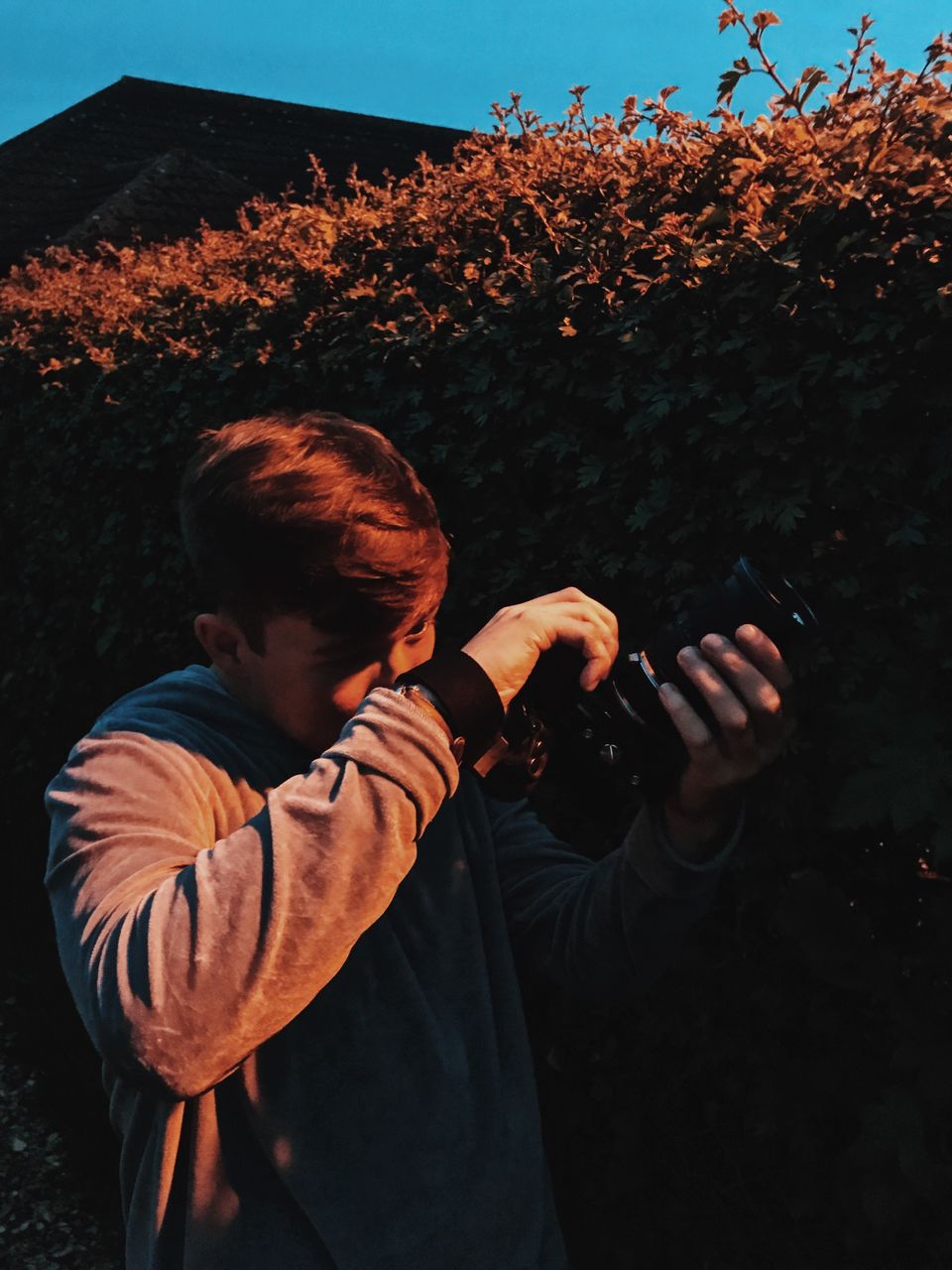 Young man holding camera while standing by plants