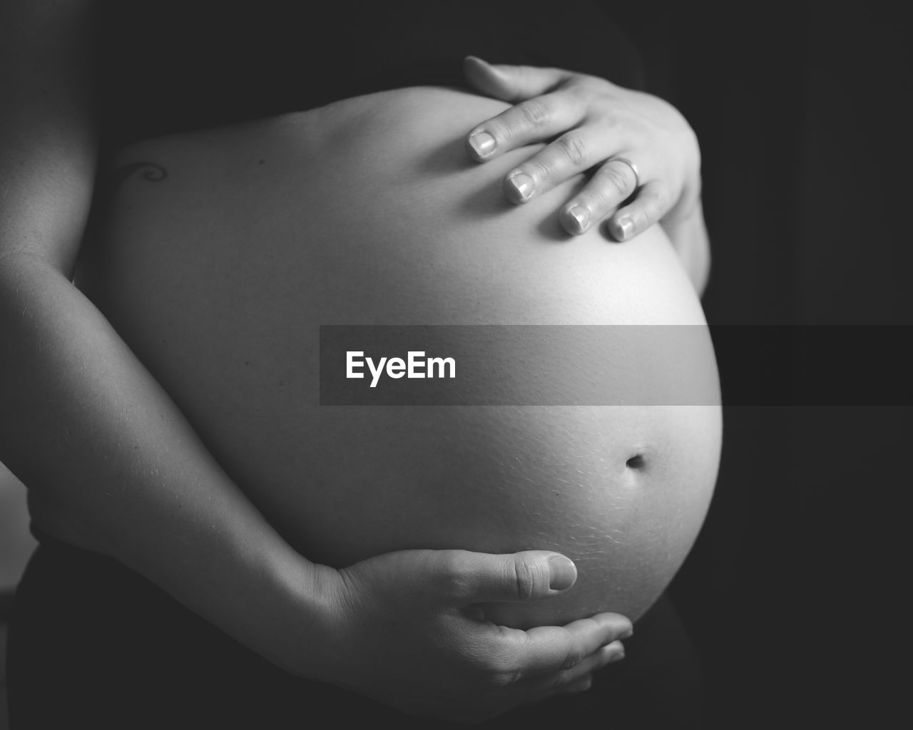 Midsection of pregnant woman standing against black background