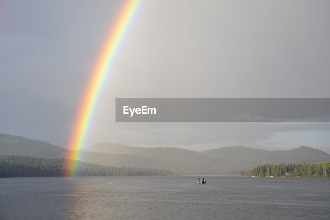 Vivid rainbow over calm lake with boat near shore in countryside