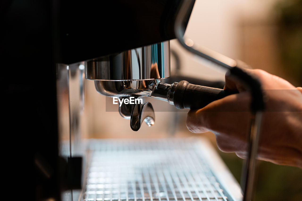 Crop anonymous barista using portafilter in coffee machine while preparing drink in cafe