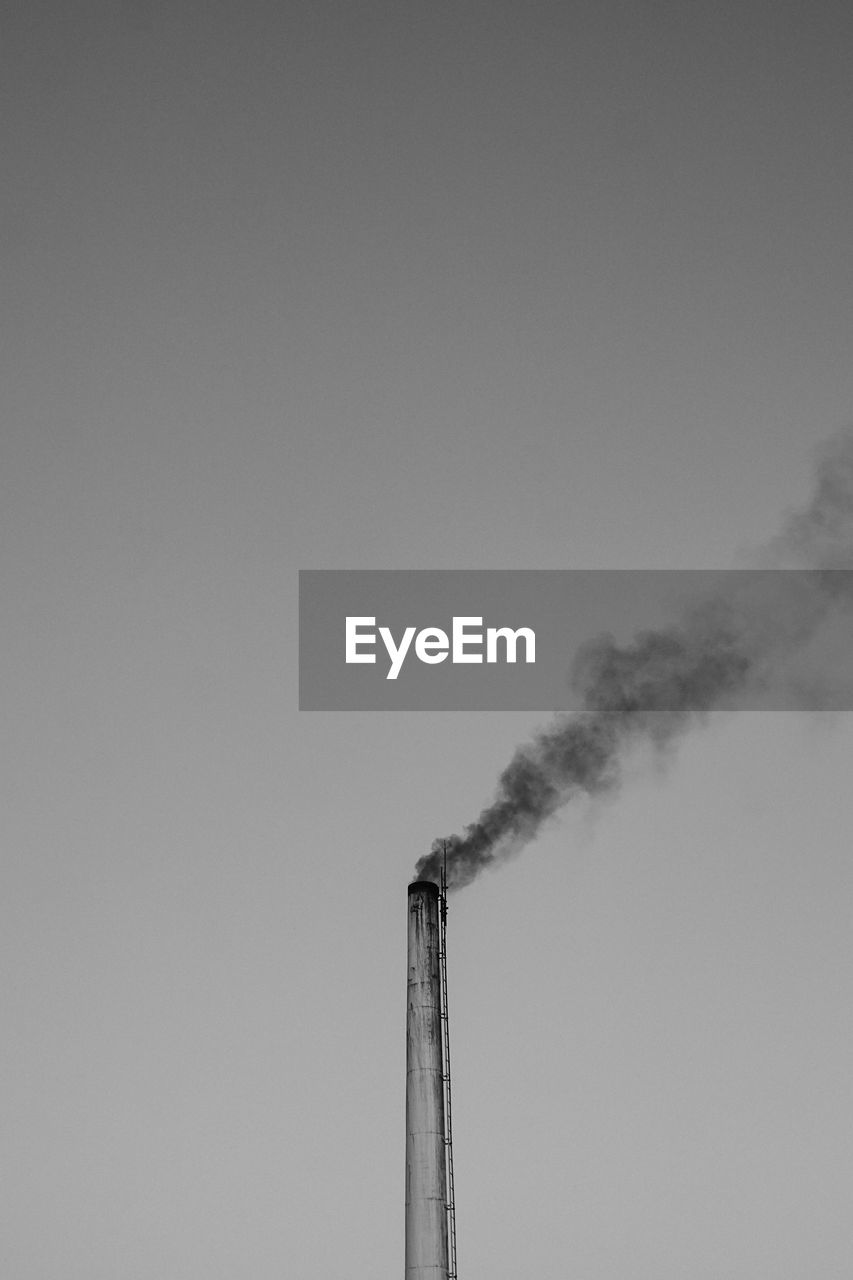 Low angle view of smoke stack emitting pollution against clear sky