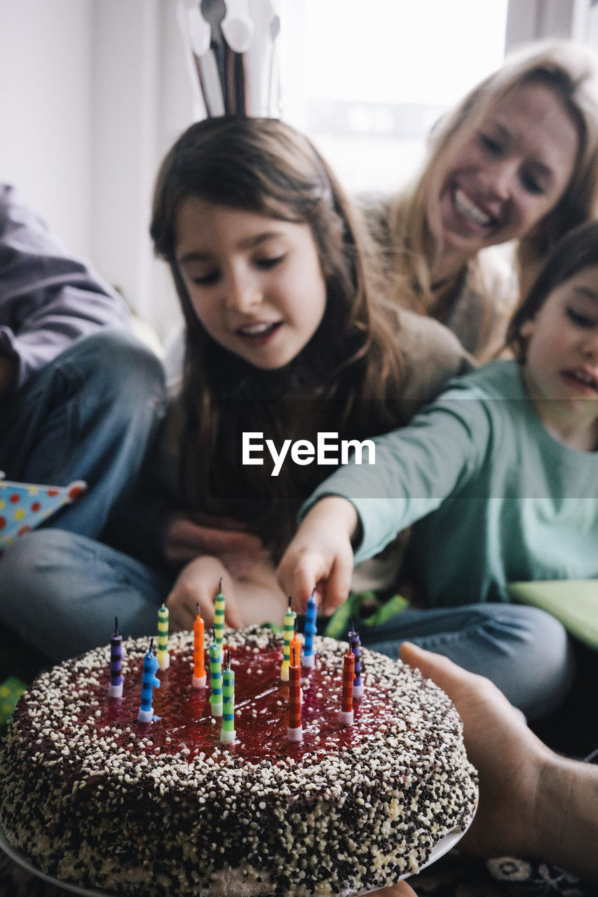 Hand of man holding birthday cake with candles against family at home