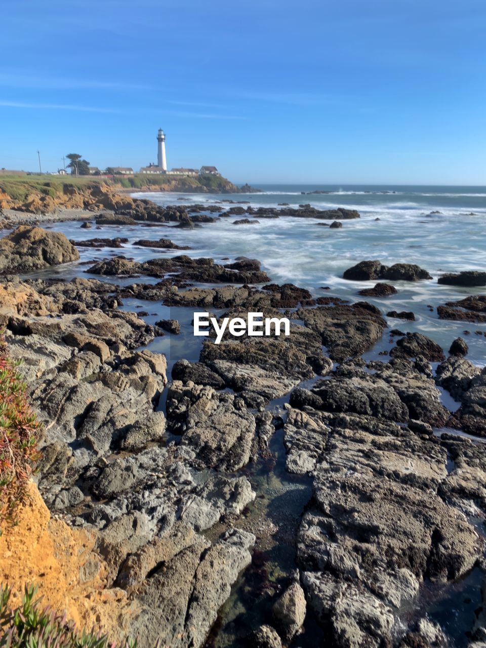 Pigeon point lighthouse from pigeon point bluffs, clear blue sky, slow shutter, on rocky coastline 