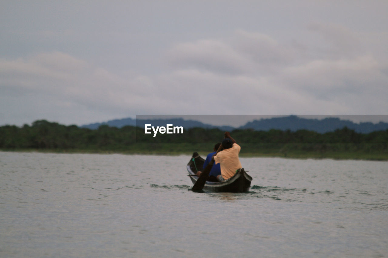 Men sitting in boat on lake against sky