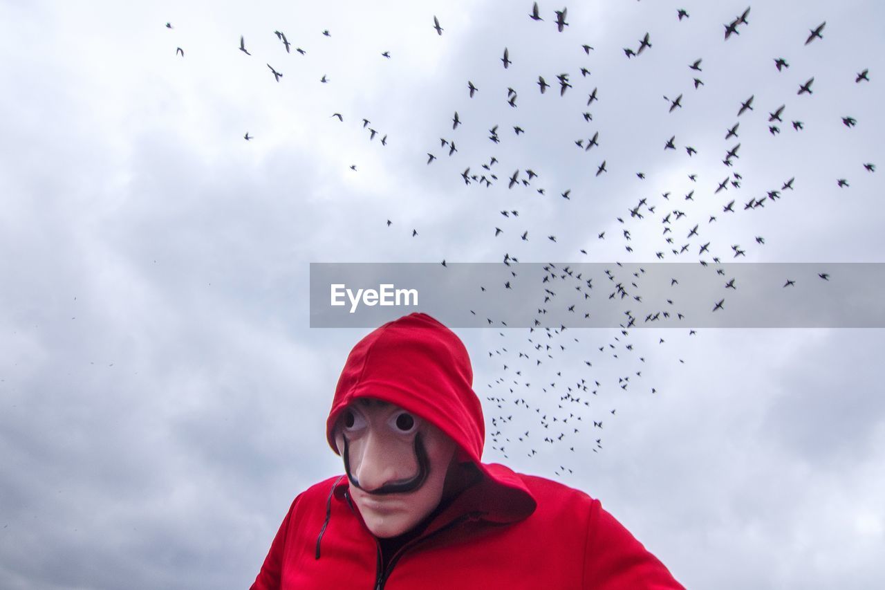 LOW ANGLE VIEW OF WOMAN LOOKING AT BIRDS AGAINST SKY