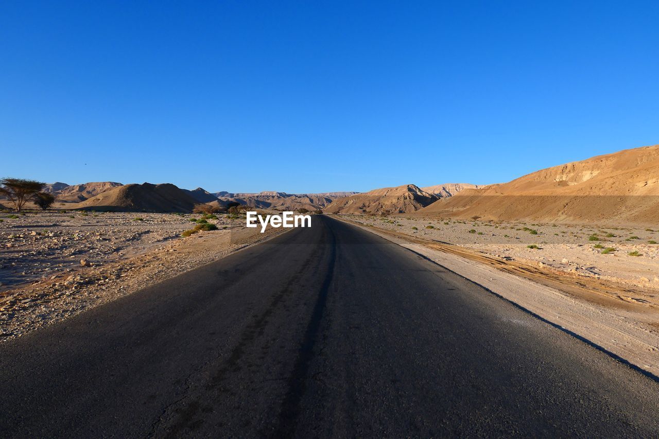 Road amidst desert against clear blue sky