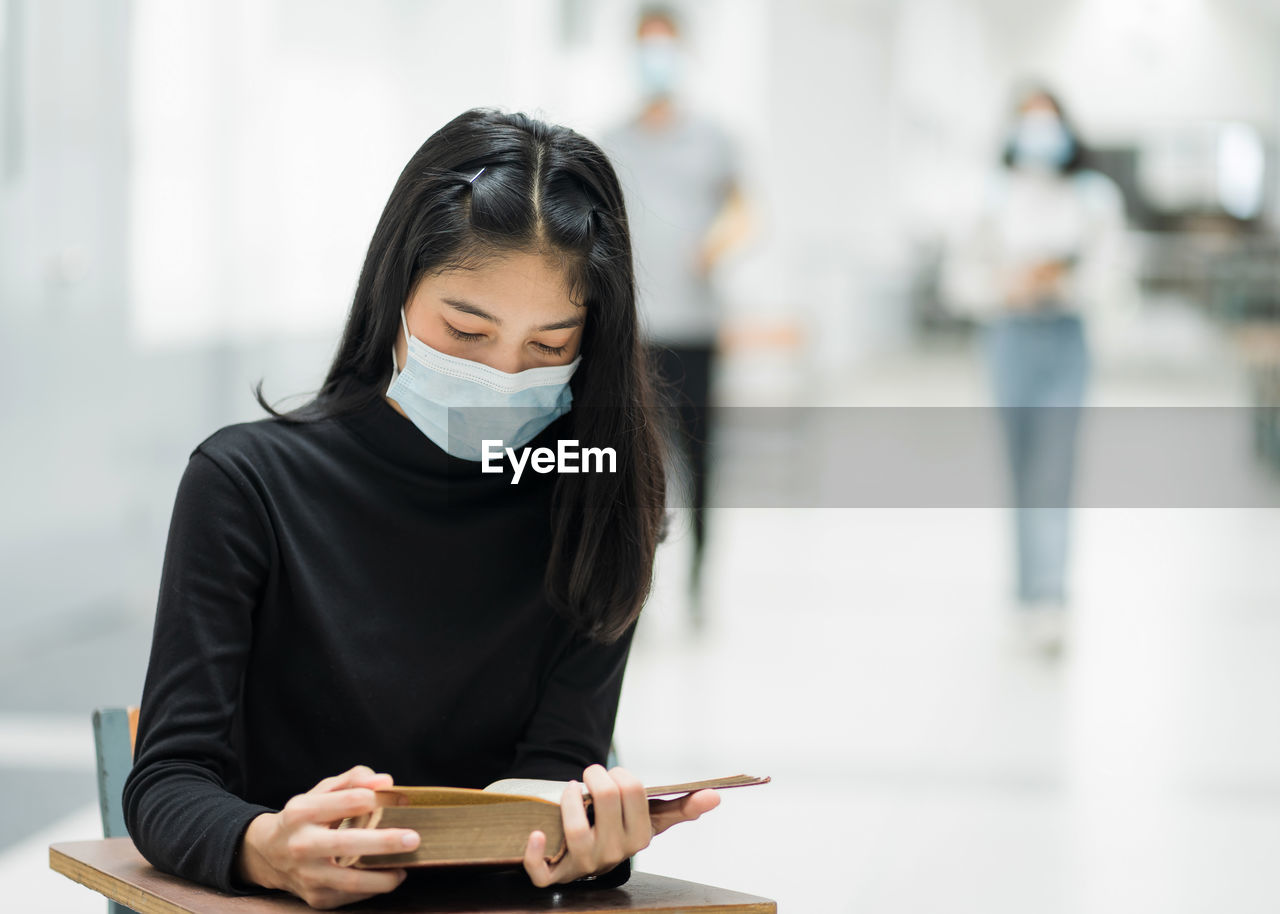 YOUNG WOMAN READING BOOK WHILE STANDING AGAINST TEXT