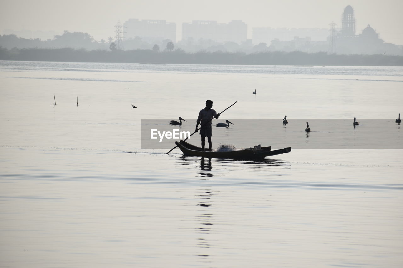 Silhouette man rowing boat in sea against sky