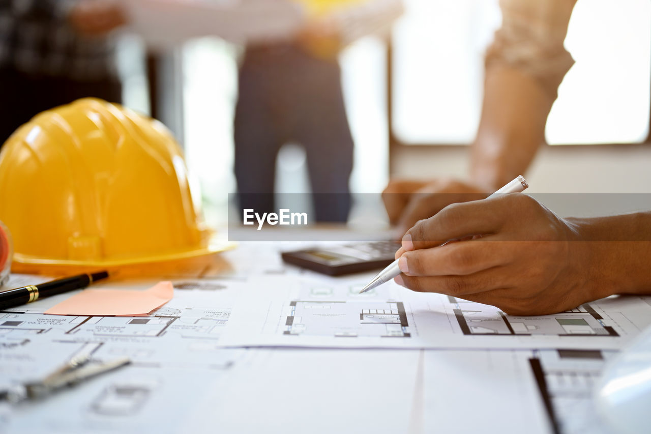 construction industry, plan, occupation, planning, adult, working, hard hat, blueprint, business, helmet, building contractor, industry, engineering, headwear, business finance and industry, person, clothing, men, hand, construction worker, indoors, businessman, manual worker, cooperation, document, technology, professional occupation, hat, construction site, teamwork, creativity, office, fashion accessory, place of work, communication, architecture, wireless technology, work helmet, white-collar worker, paper, development, table, computer, selective focus, businesswoman, meeting, women, young adult, corporate business, expertise