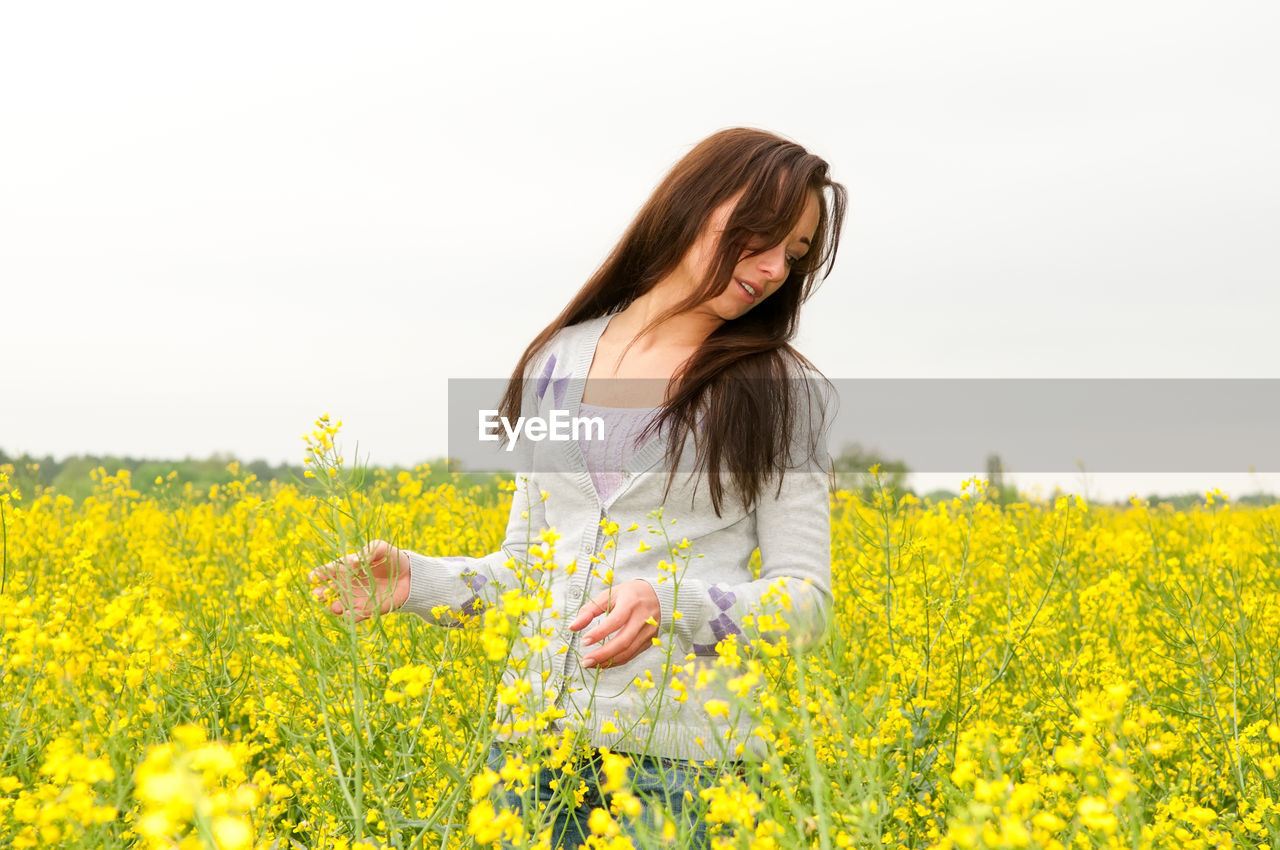Woman standing at rape field against clear sky