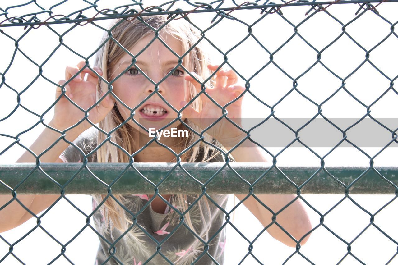 Portrait of girl making face seen through chainlink fence