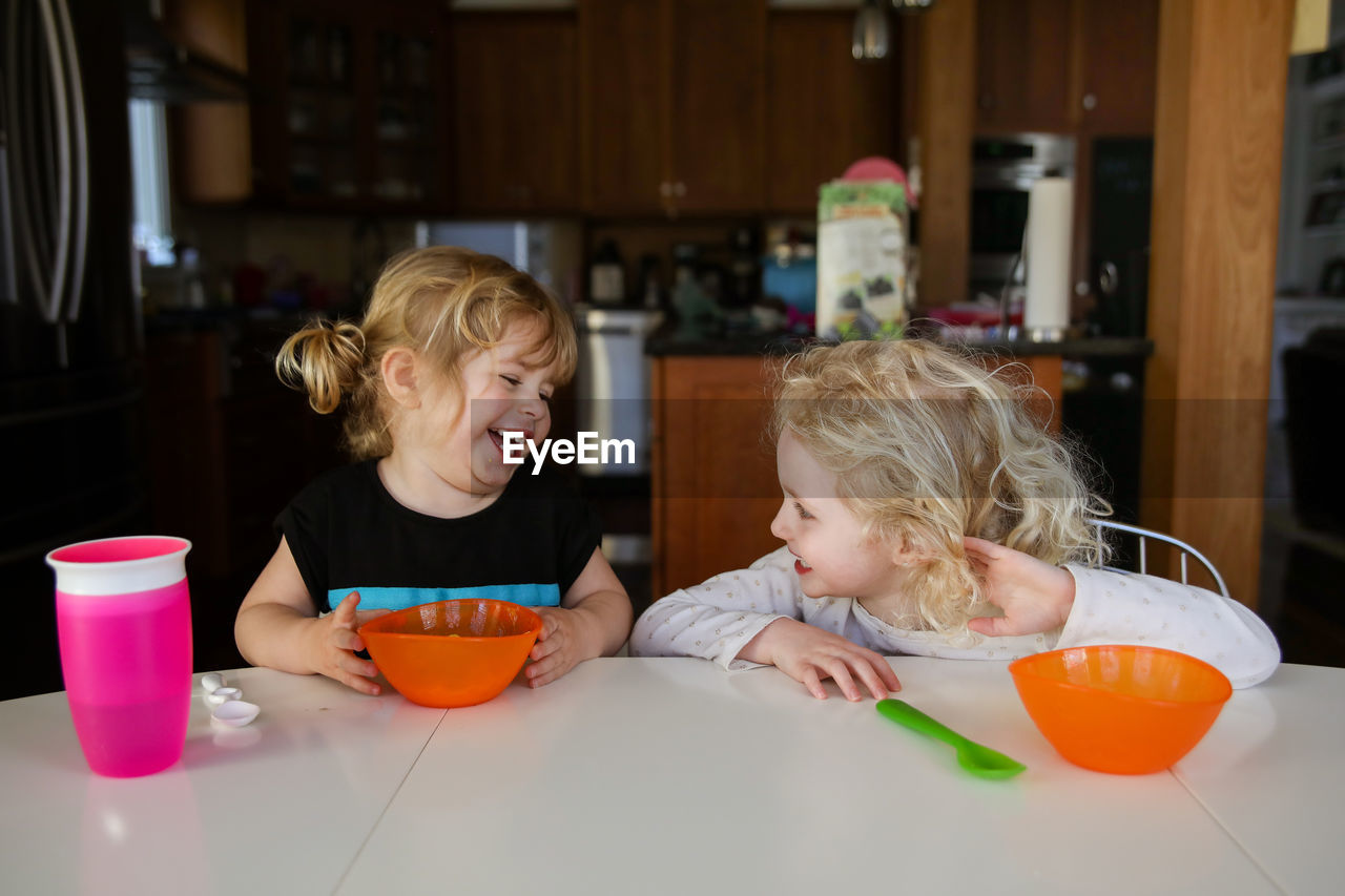 Cheerful sisters talking while sitting at dining table