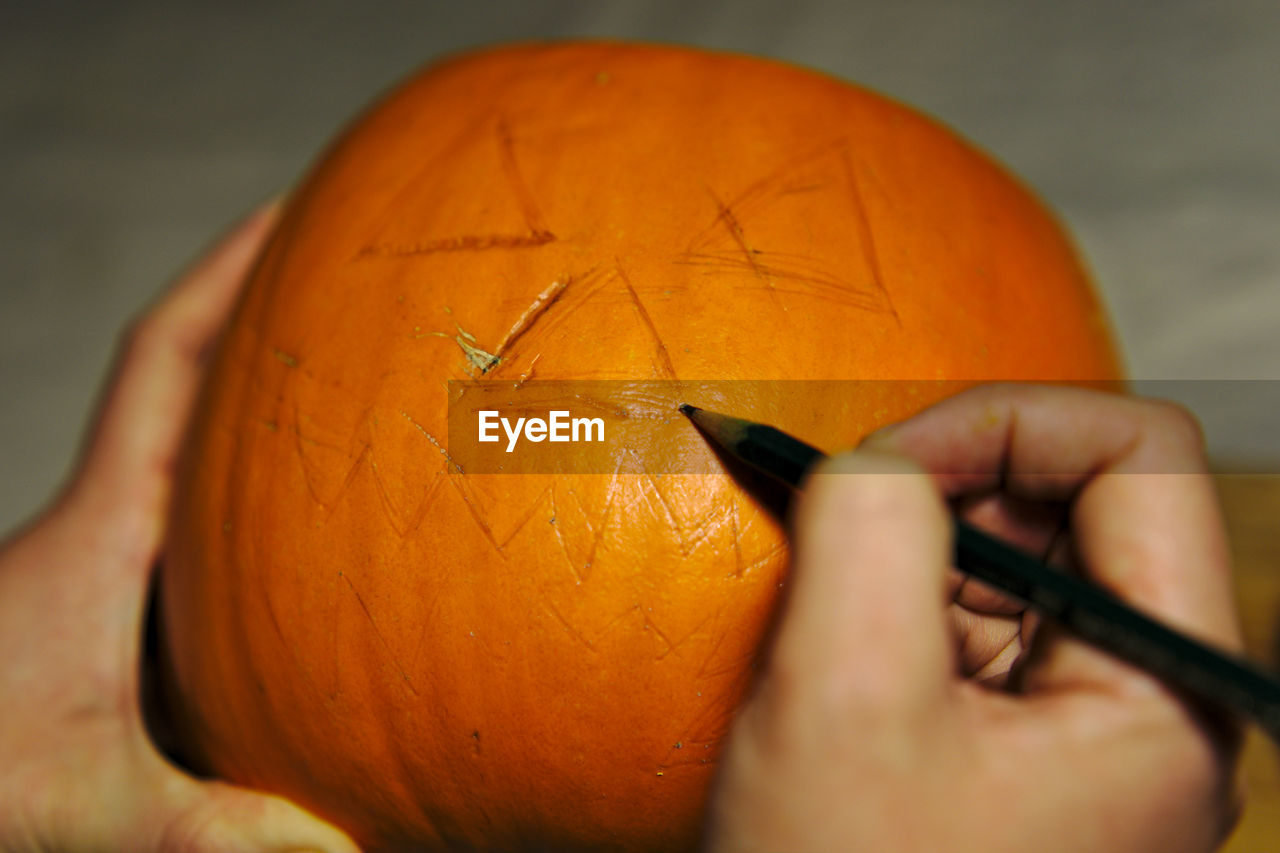 Cropped hands marking on pumpkin during halloween