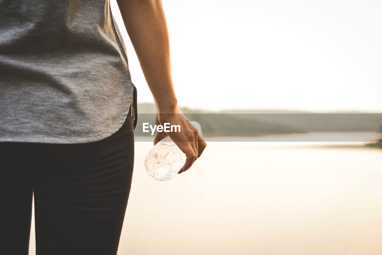 Cropped image of woman water bottle while standing against river