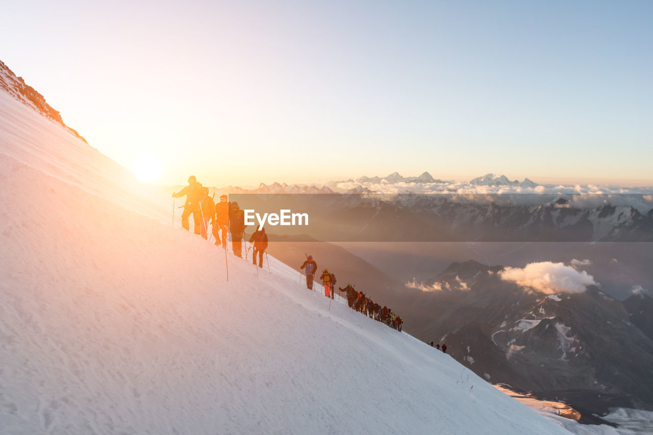 People climbing on snowcapped mountain against sky