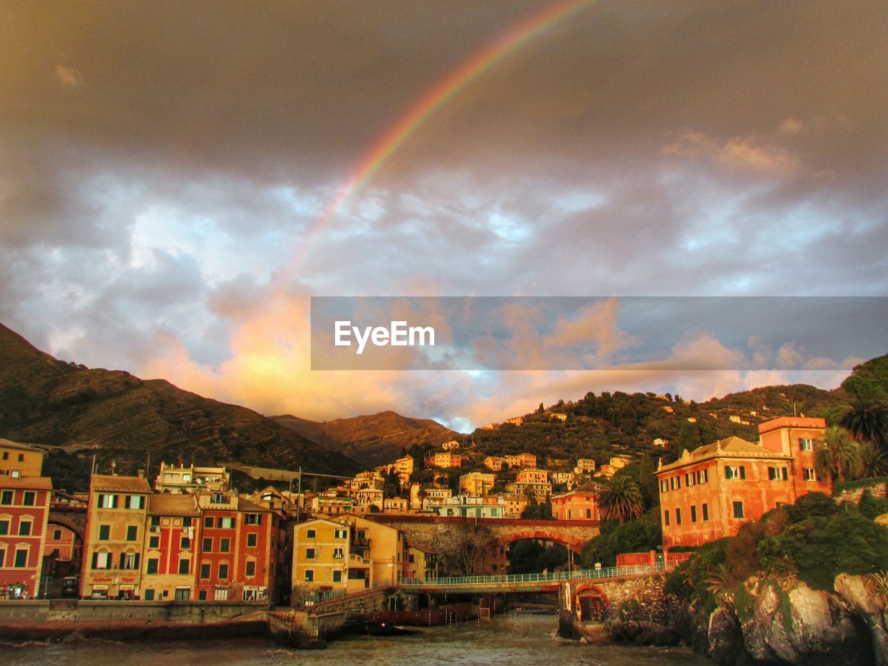 Low angle view of town against rainbow during sunset