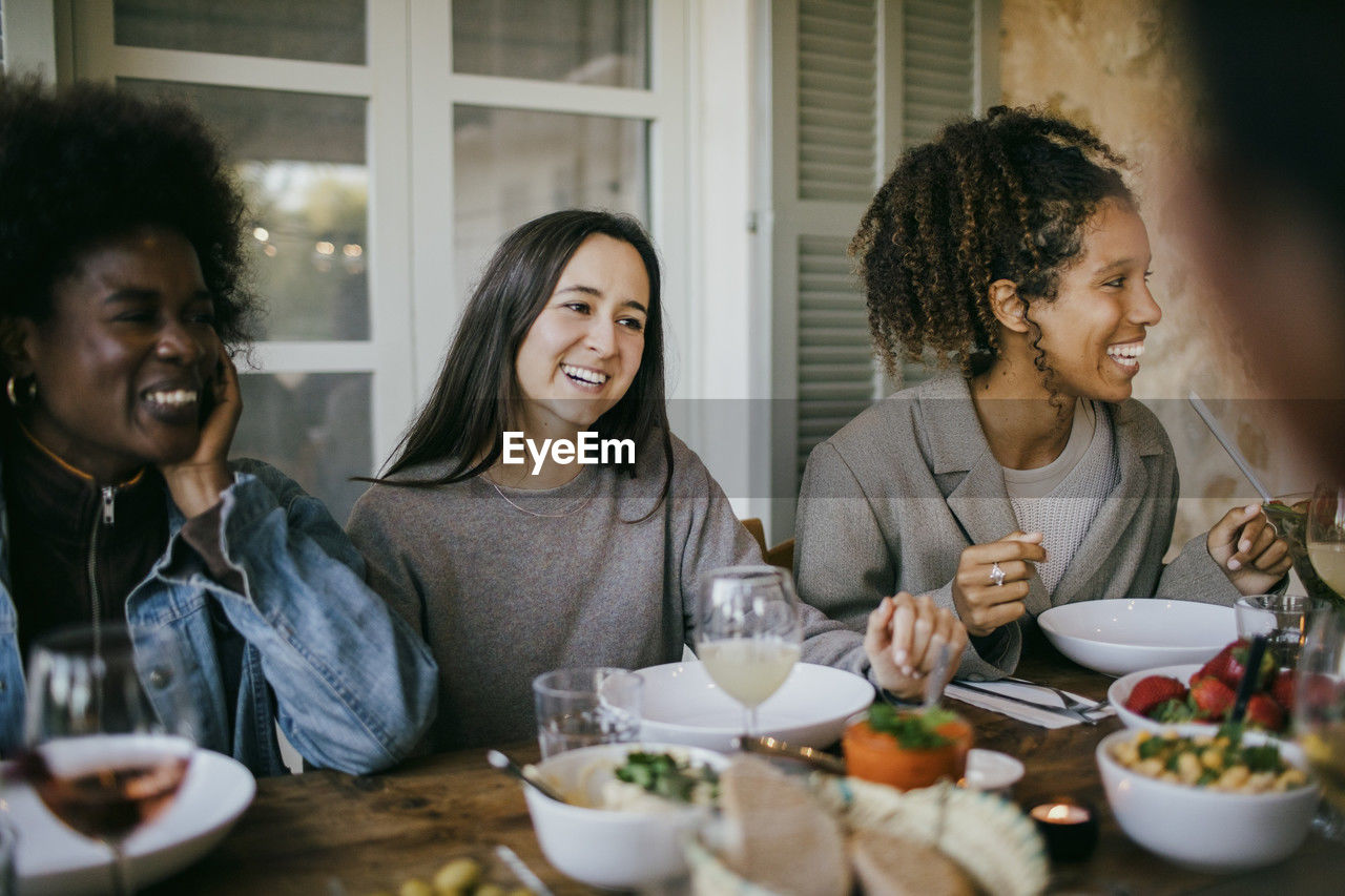 Happy female friends sitting together at dining table enjoying dinner in patio