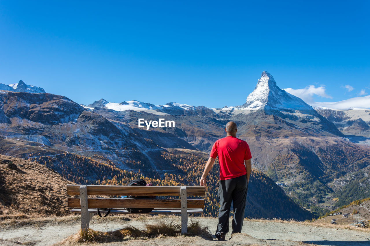 Rear view of man standing against snowcapped mountain and sky