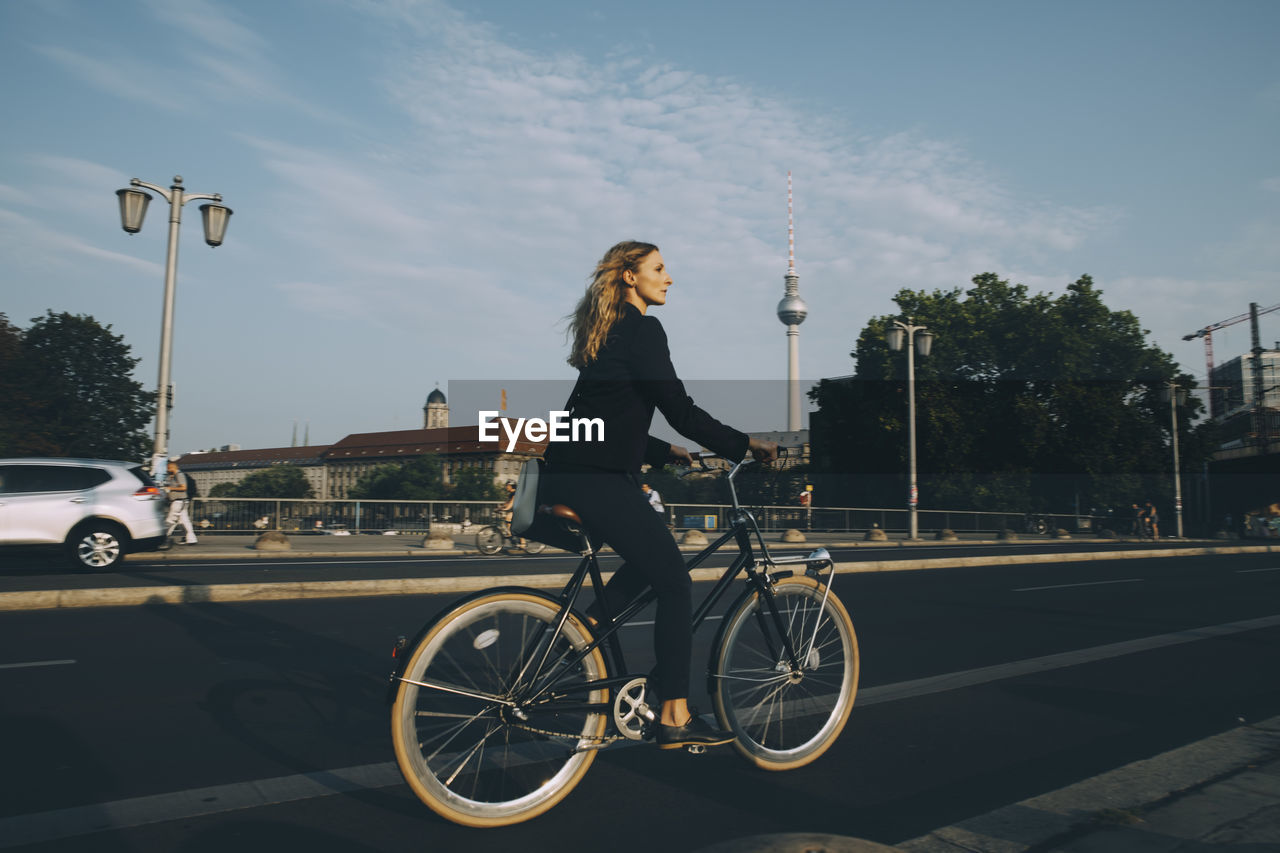 Side view of businesswoman riding bicycle on street in city