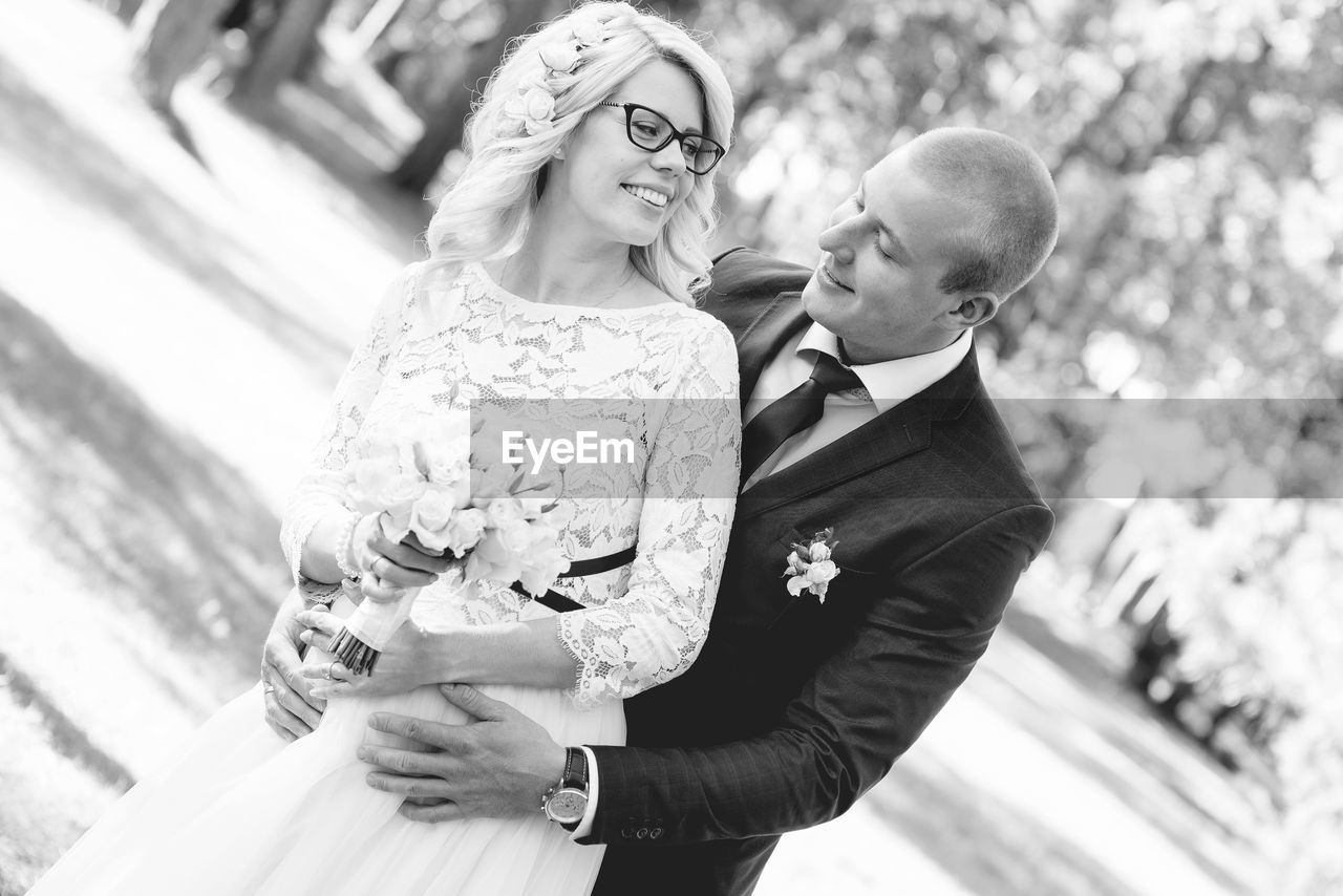 Bride and bridegroom standing against trees at park