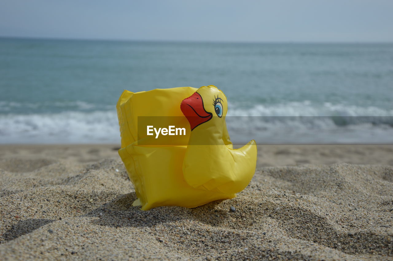 sea, beach, water, land, horizon over water, yellow, horizon, sand, toy, nature, wave, sky, animal representation, no people, plastic, holiday, animal, day, beauty in nature, bird, representation, ocean, outdoors, shore, focus on foreground, motion, vacation, trip
