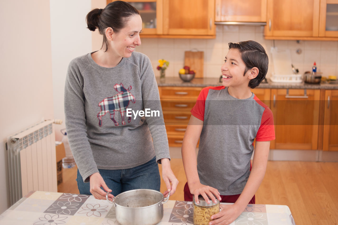 Smiling mother teaching son while preparing food at home