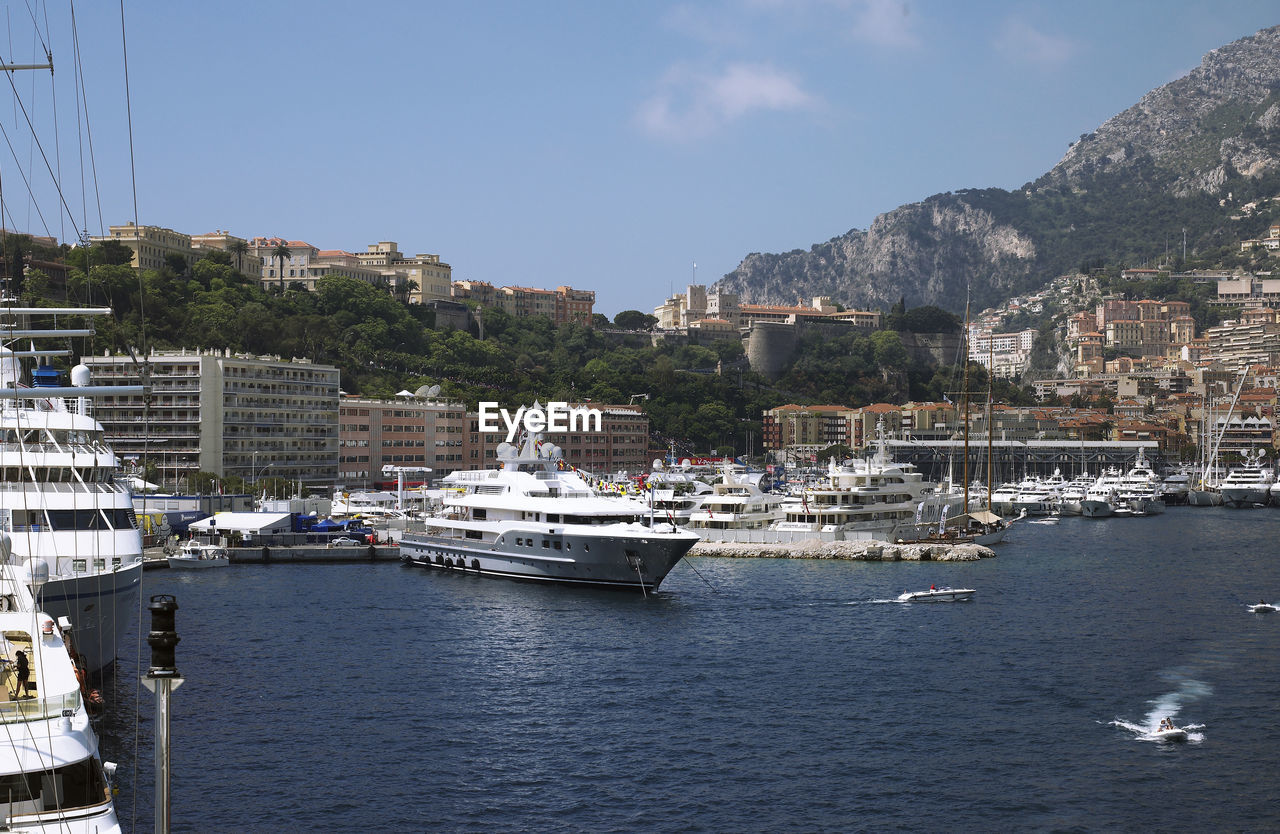 SAILBOATS MOORED IN SEA BY BUILDINGS AGAINST SKY