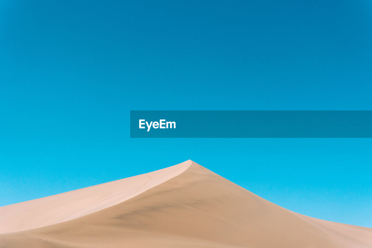 Low angle view of sand dunes against clear blue sky