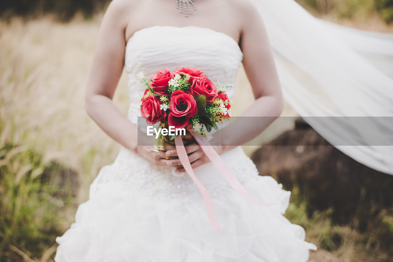 Midsection of bride holding rose bouquet while standing on field