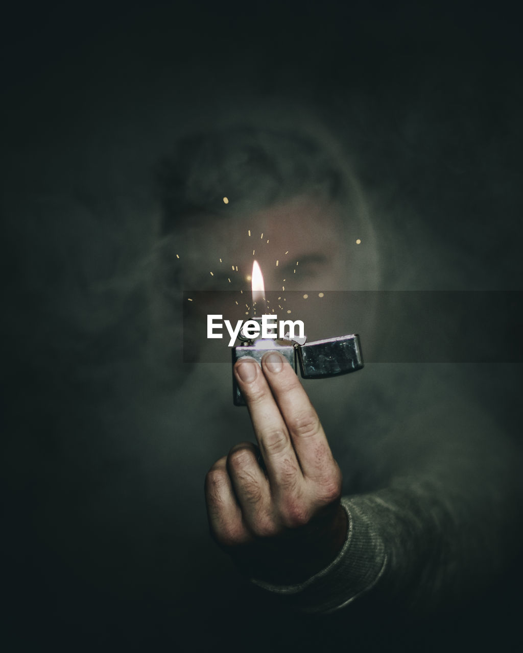 Close-up of man holding burning cigarette lighter amidst smoke