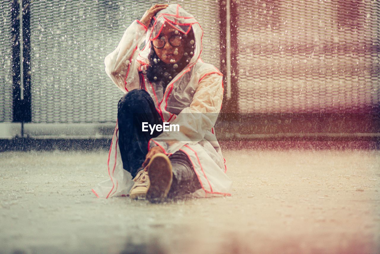 Woman in raincoat sitting on the floor in the rain. 