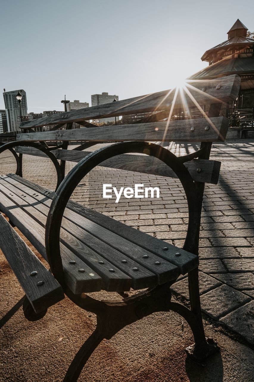 Empty bench against clear sky on sunny day